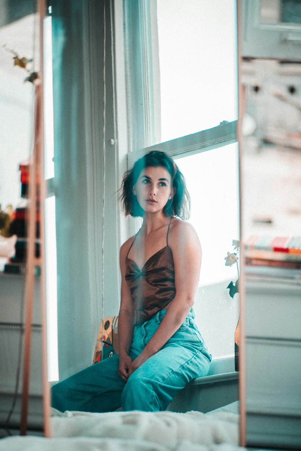 woman in brown spaghetti strap top and blue denim jeans sitting on white wooden framed glass