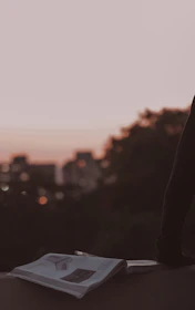 An open book resting on an old wooden table, with a backdrop of a futuristic city skyline at dusk.