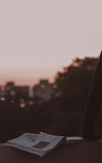 An open book resting on an old wooden table, with a backdrop of a futuristic city skyline at dusk.