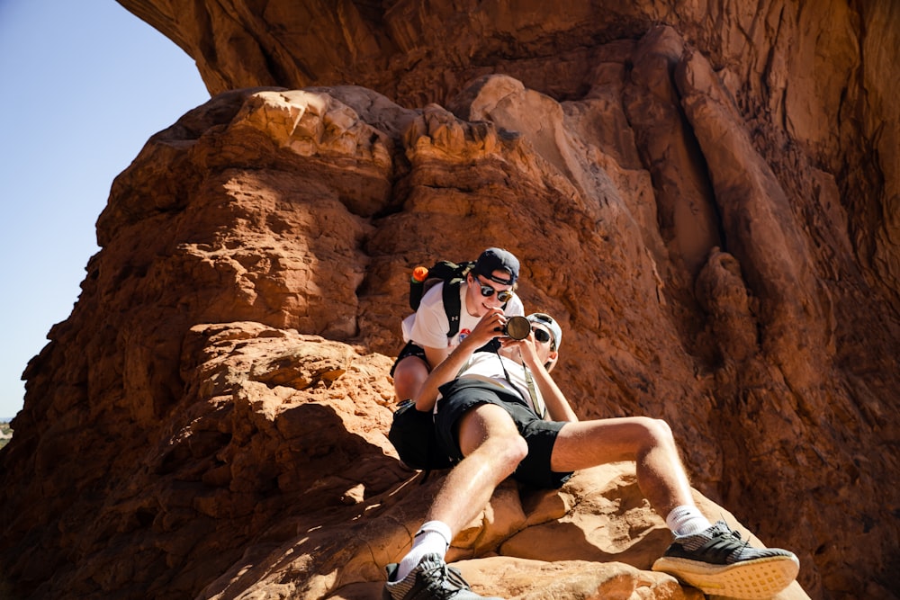 woman in white tank top and black shorts sitting on brown rock formation during daytime