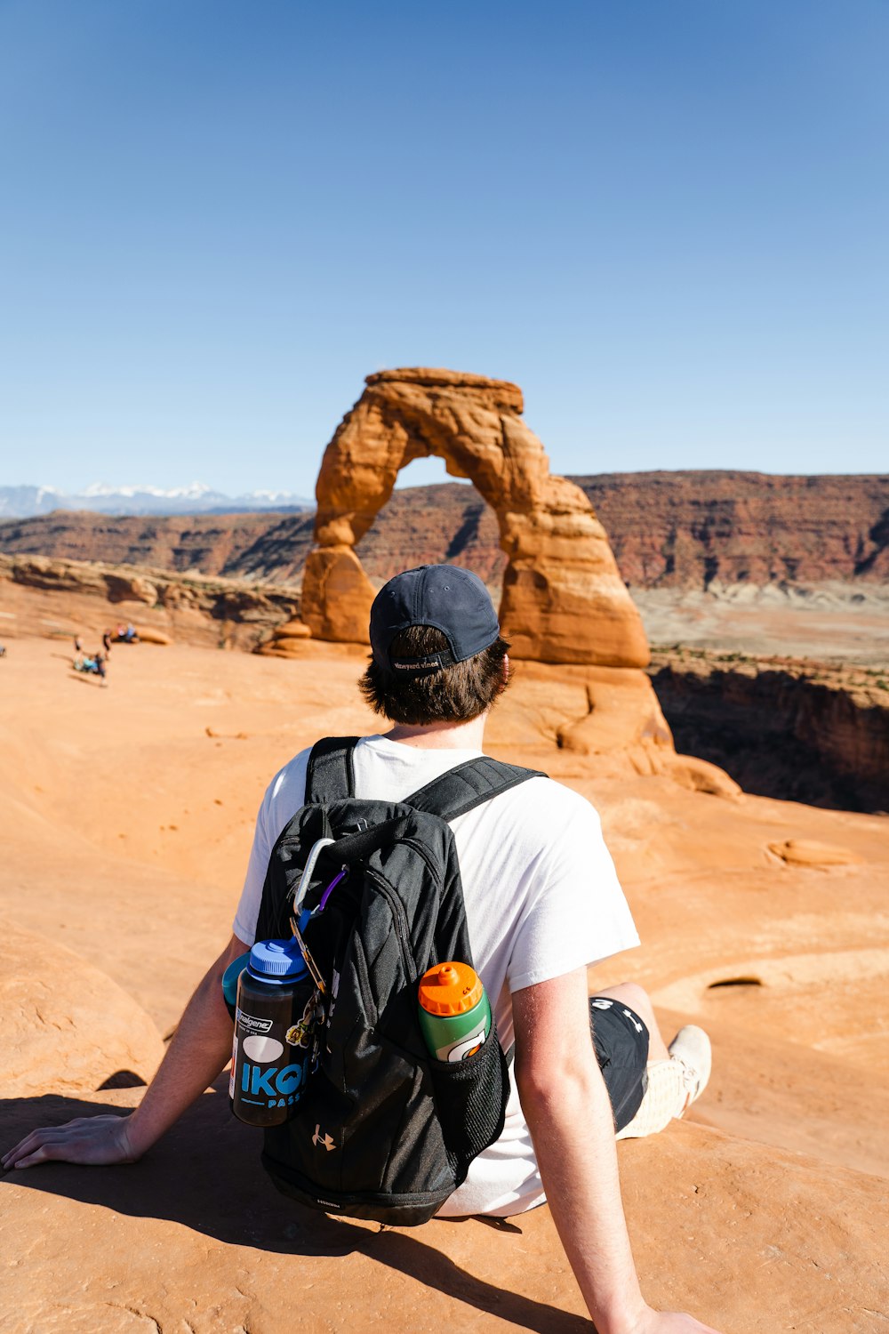 man in white t-shirt wearing black backpack standing on brown rock formation during daytime