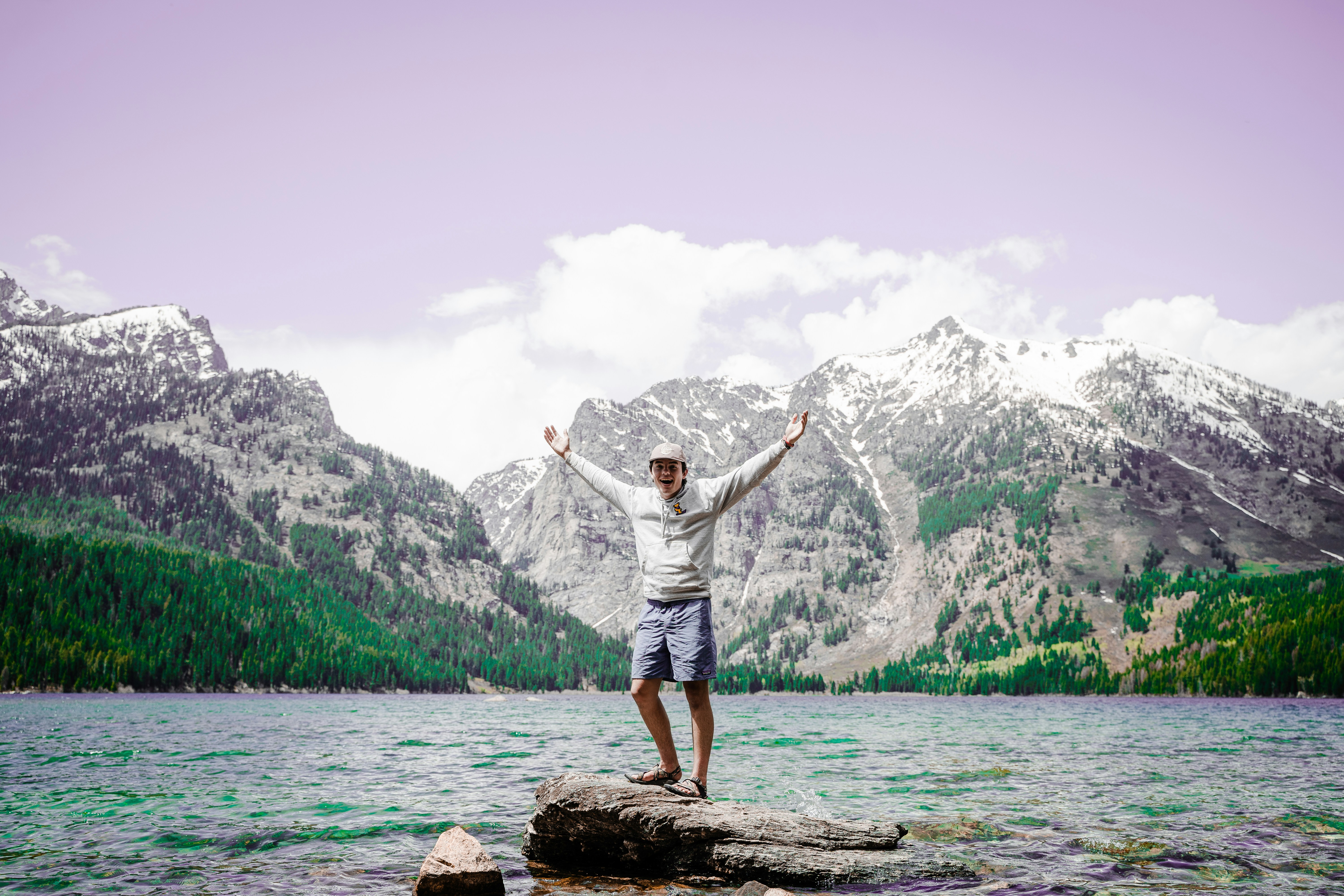 man in white shirt standing on brown rock near body of water during daytime