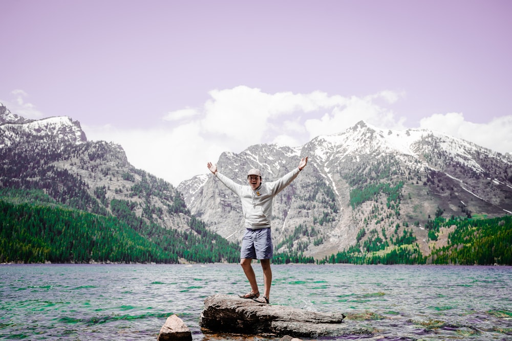 man in white shirt standing on brown rock near body of water during daytime