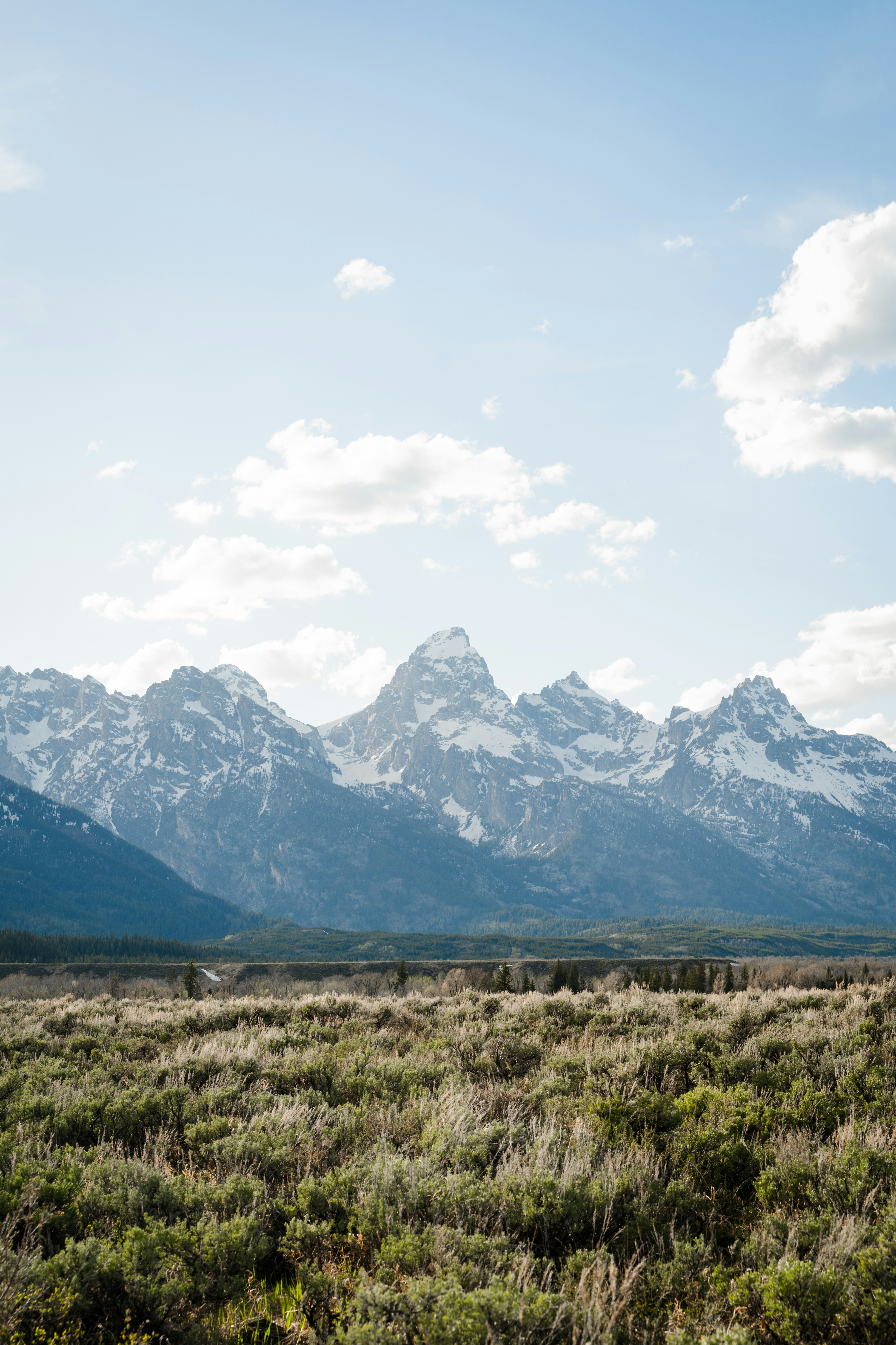 green grass field near mountain under white clouds during daytime