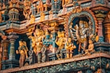A richly detailed facade of a Hindu temple features an array of colorful, ornate sculptures depicting various deities and figures. The intricate carvings and vibrant colors create a mesmerizing visual effect, showcasing traditional Indian art styles.
