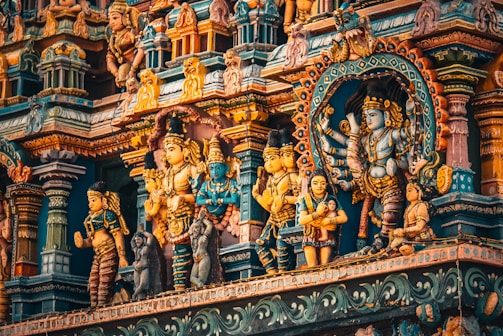 A richly detailed facade of a Hindu temple features an array of colorful, ornate sculptures depicting various deities and figures. The intricate carvings and vibrant colors create a mesmerizing visual effect, showcasing traditional Indian art styles.