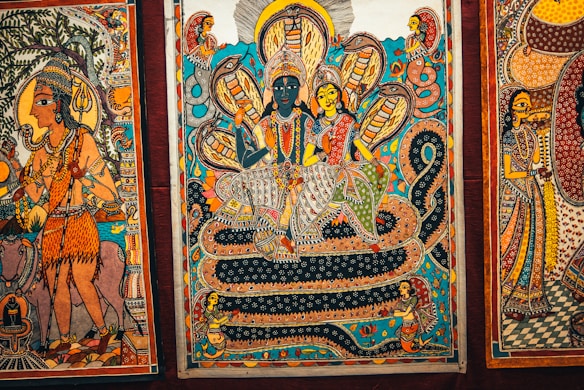 A traditional Indian painting depicting mythological figures and serpentine forms. Intricate patterns and vibrant colors are prominent, featuring deities seated on a coiled serpent, surrounded by smaller figures and mystical motifs.