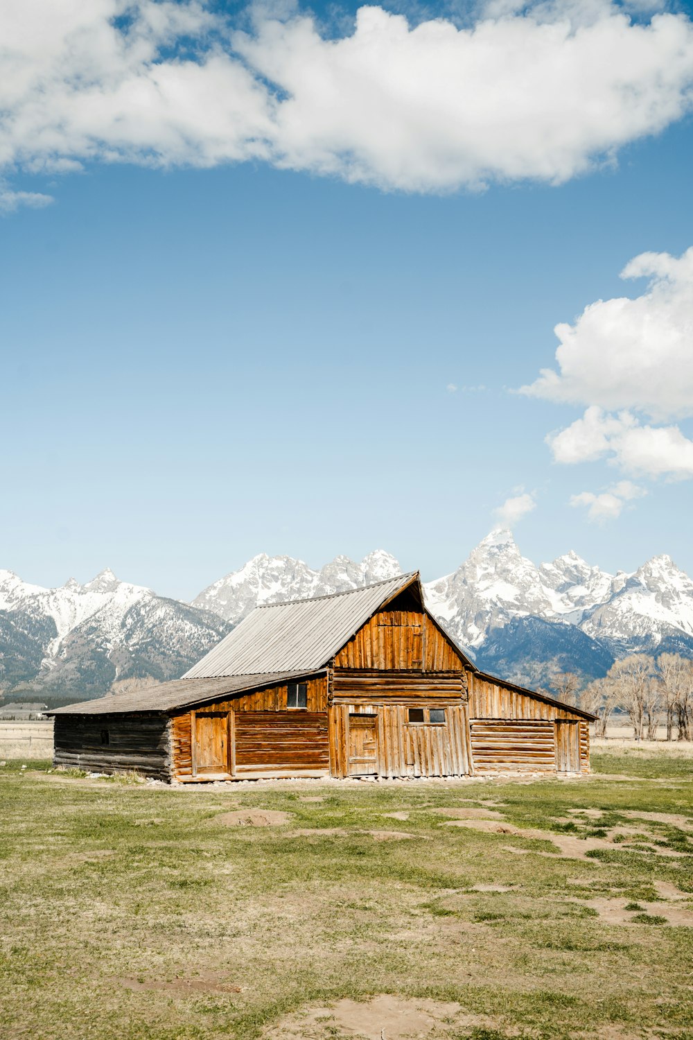 brown wooden barn near snow covered mountain under blue sky during daytime