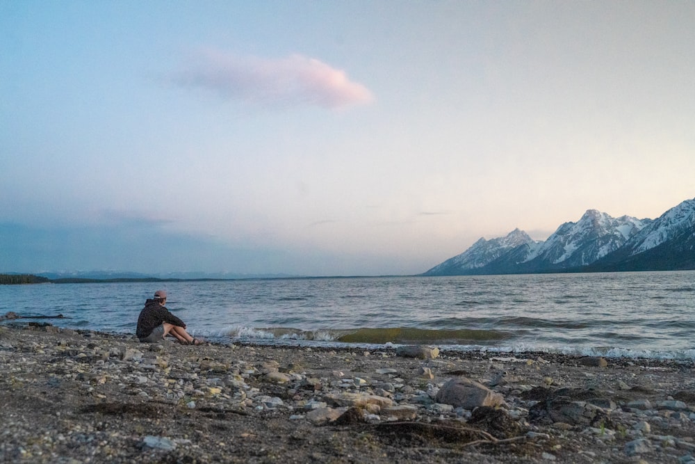 man sitting on rock near sea during daytime