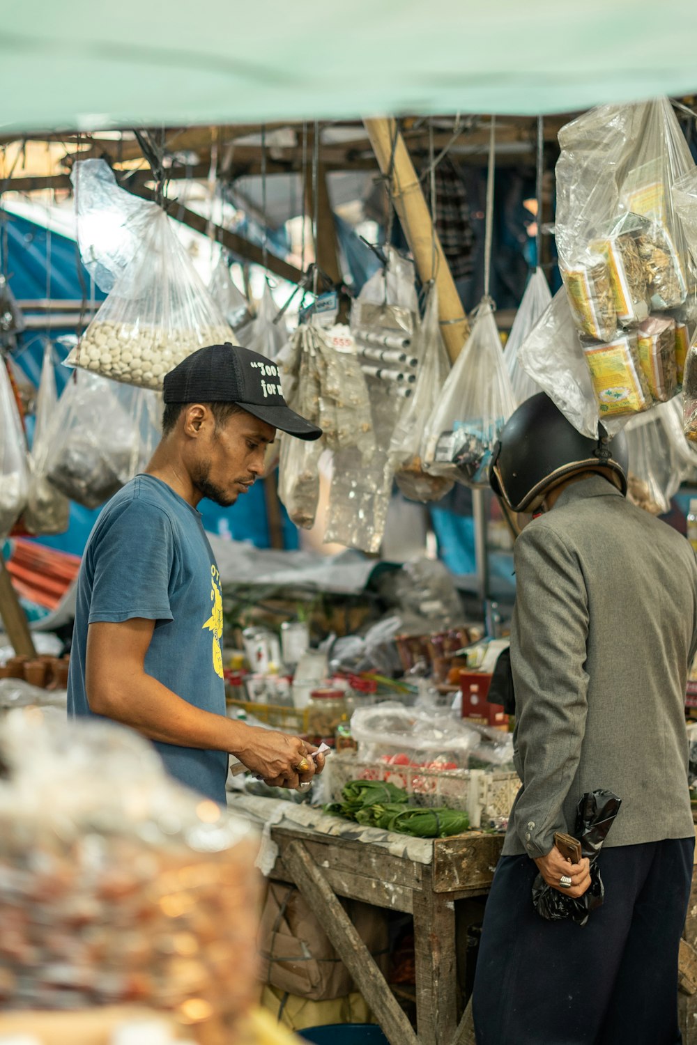 man in blue crew neck t-shirt and gray pants standing in front of vegetable stand