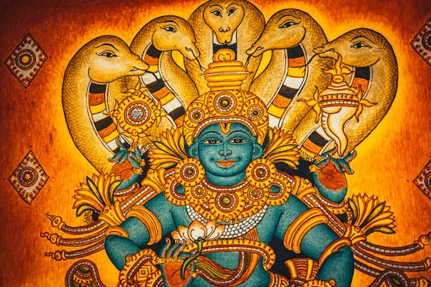 A traditional Indian artwork depicting a deity with blue skin adorned in intricate golden jewelry and ornaments, surrounded by multiple hooded cobras. The background features warm shades of orange and gold, adding to the mythical and spiritual ambiance.