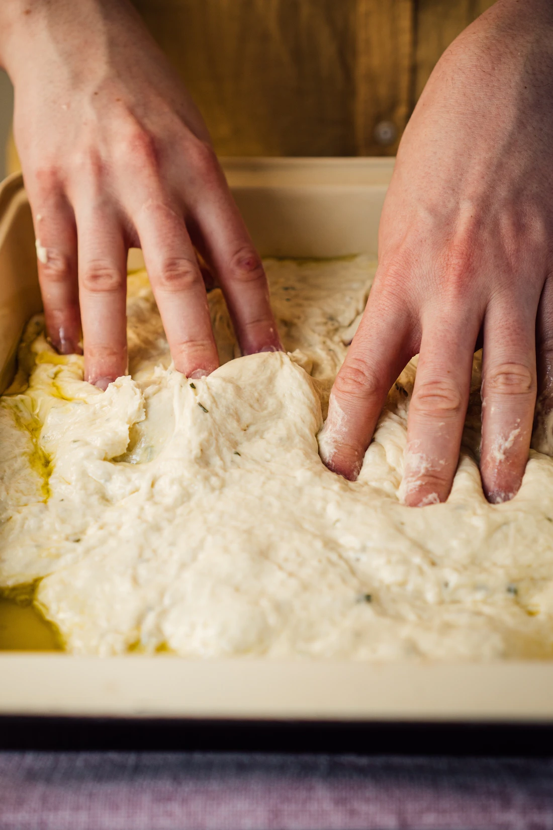 Hands folding a soft, wet dough in a tub