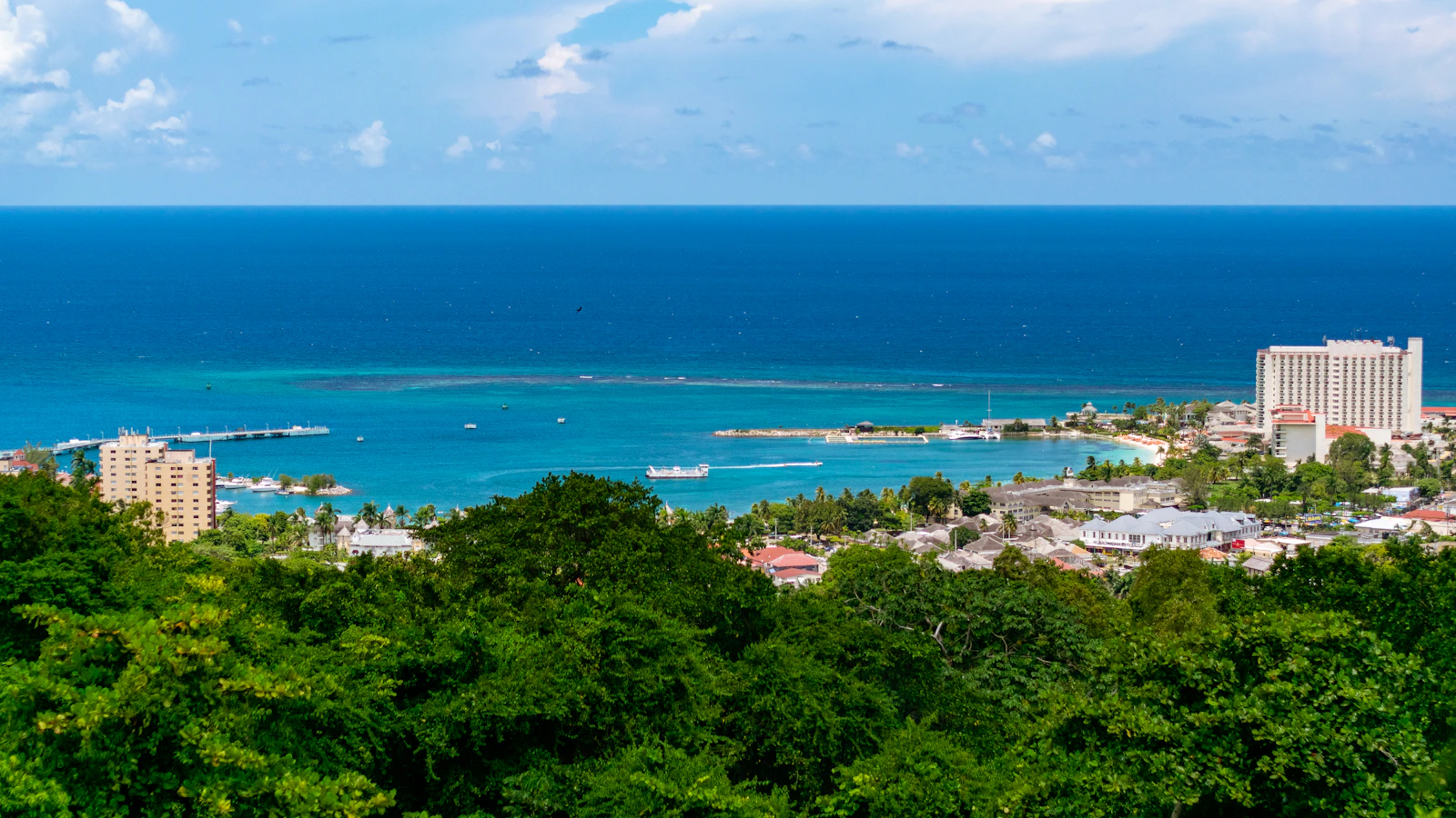 Aerial view of a Caribbean harbour town with turquoise water, green hills and a coastline, representing the region the Caribbean AI Task Force's final report covers