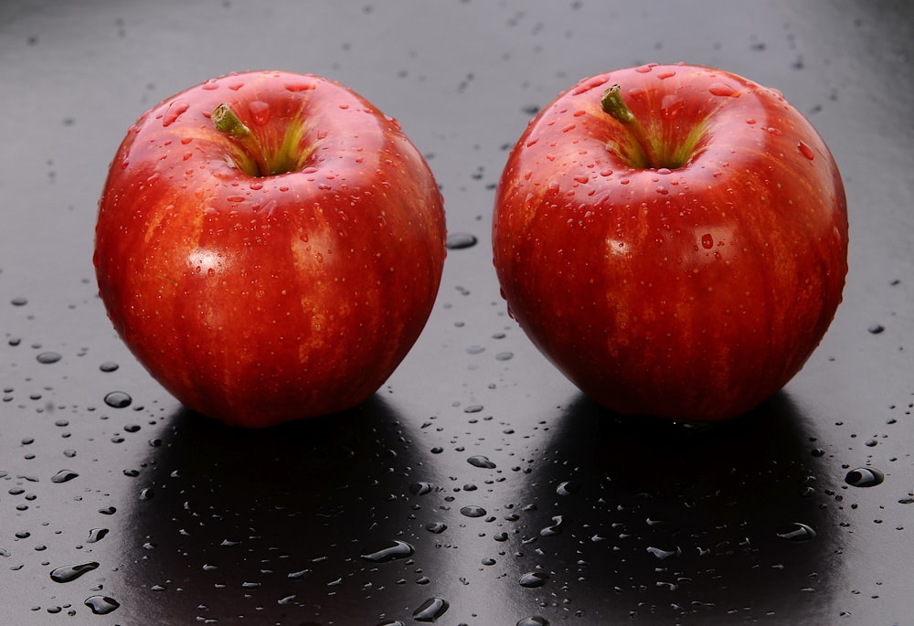 2 red apples on black surface