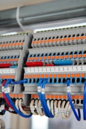 A detailed view of a terminal block with several rows of connections, featuring orange and grey components with numerous blue and white wires organized neatly. Each wire is labeled with a clear identification number. The photo captures the intricate layout and structured organization of electrical components.