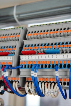 A detailed view of a terminal block with several rows of connections, featuring orange and grey components with numerous blue and white wires organized neatly. Each wire is labeled with a clear identification number. The photo captures the intricate layout and structured organization of electrical components.