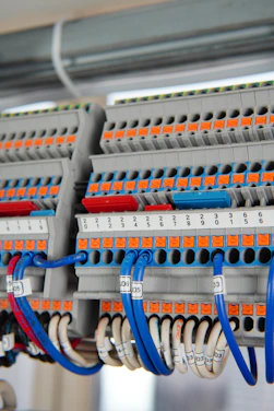 A detailed view of a terminal block with several rows of connections, featuring orange and grey components with numerous blue and white wires organized neatly. Each wire is labeled with a clear identification number. The photo captures the intricate layout and structured organization of electrical components.