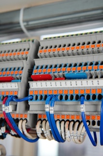 A detailed view of a terminal block with several rows of connections, featuring orange and grey components with numerous blue and white wires organized neatly. Each wire is labeled with a clear identification number. The photo captures the intricate layout and structured organization of electrical components.