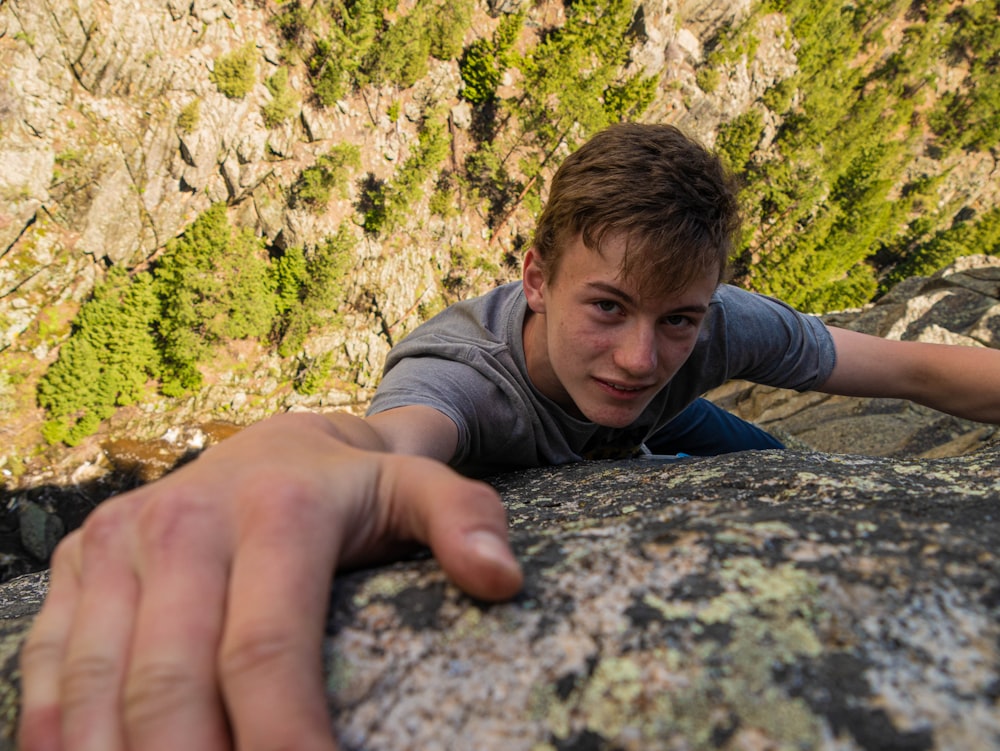 boy in gray hoodie lying on gray rock during daytime