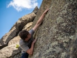 Close-up of chalked hands gripping rough rock against a clear blue sky.