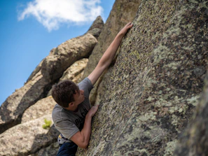 A climber gripping a rugged rock face with a clear blue sky overhead.