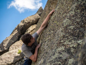 Climber gripping a rugged rock face under a clear blue sky