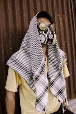 fine art photography,how to photograph fine art portrait of a male model wearing strange mask and steampunk glasses and a palastenian scarf.; man in blue white and brown plaid button up shirt wearing brown leather face mask