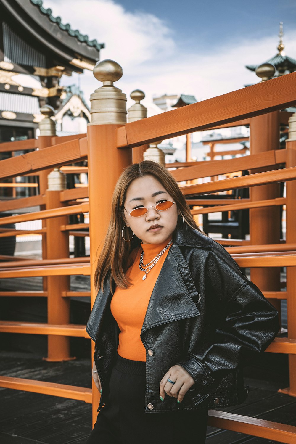 woman in black leather jacket standing beside brown wooden railings during daytime