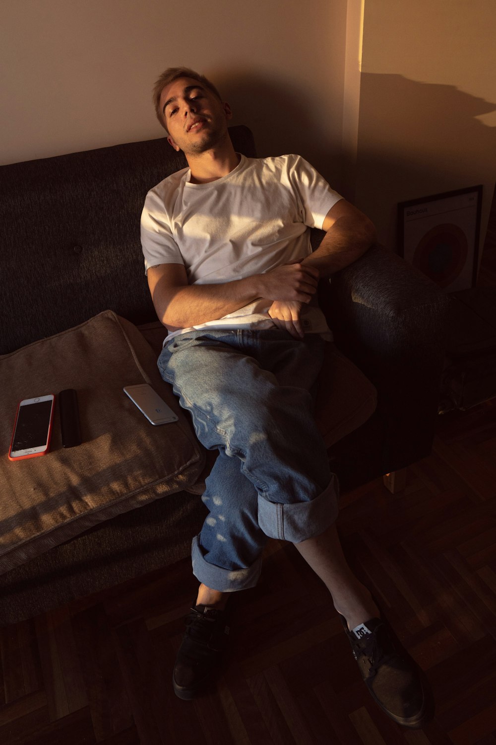 Mann in weißem Rundhals-T-Shirt und blauer Jeans sitzt auf schwarzer Couch