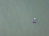 Two paddleboards float on a vast, calm expanse of water. Each board is occupied by a person, and the boards are tethered together. The water's surface is smooth, and its color is a muted green, creating a serene atmosphere.