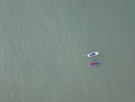 Two paddleboards float on a vast, calm expanse of water. Each board is occupied by a person, and the boards are tethered together. The water's surface is smooth, and its color is a muted green, creating a serene atmosphere.