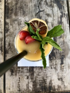 A refreshing beverage with fruits and herbs served in an aesthetic glass.