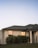 Modern luxury home exterior with large windows and landscaped garden at sunset.
