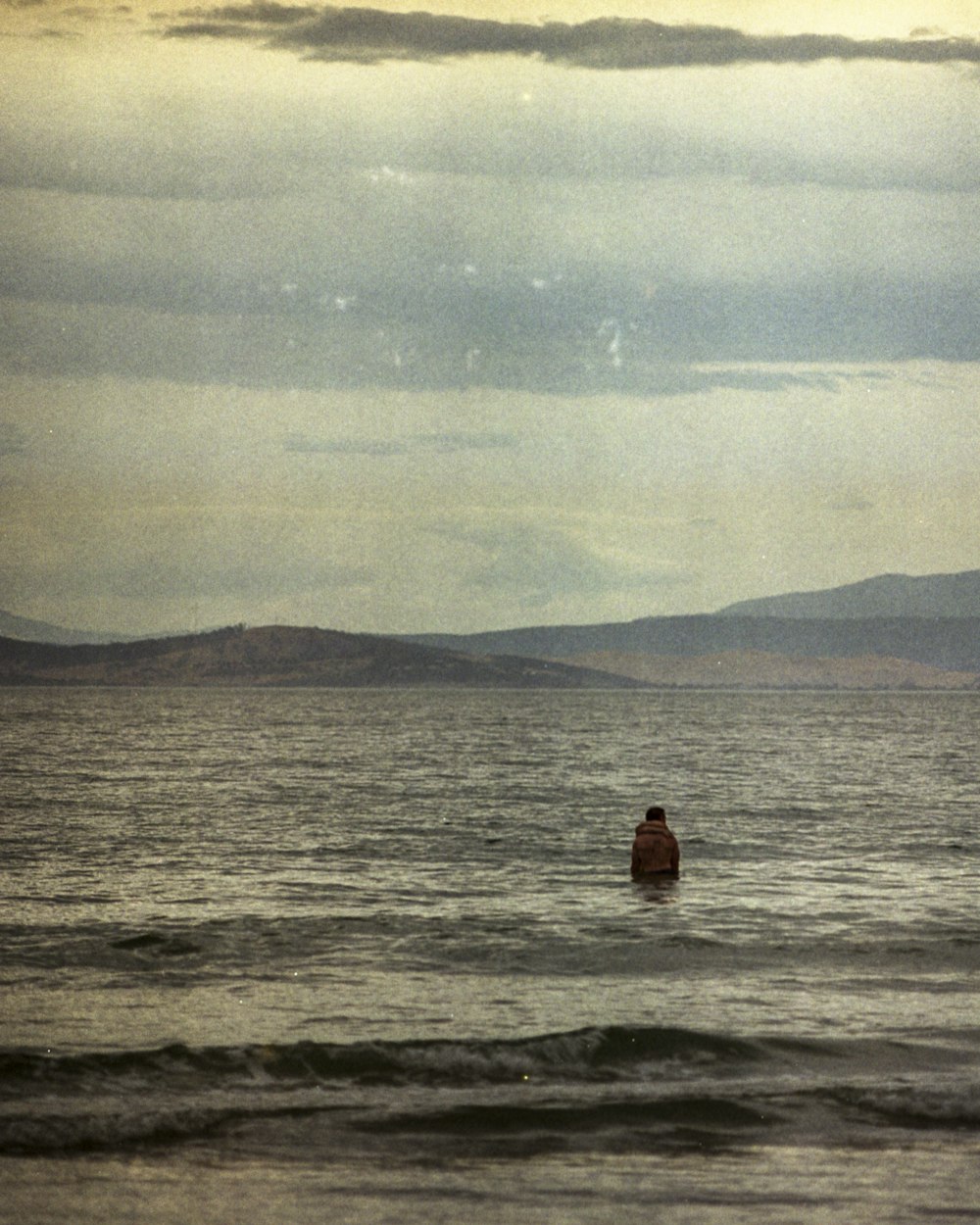 person in red hoodie sitting on brown rock in front of body of water during daytime
