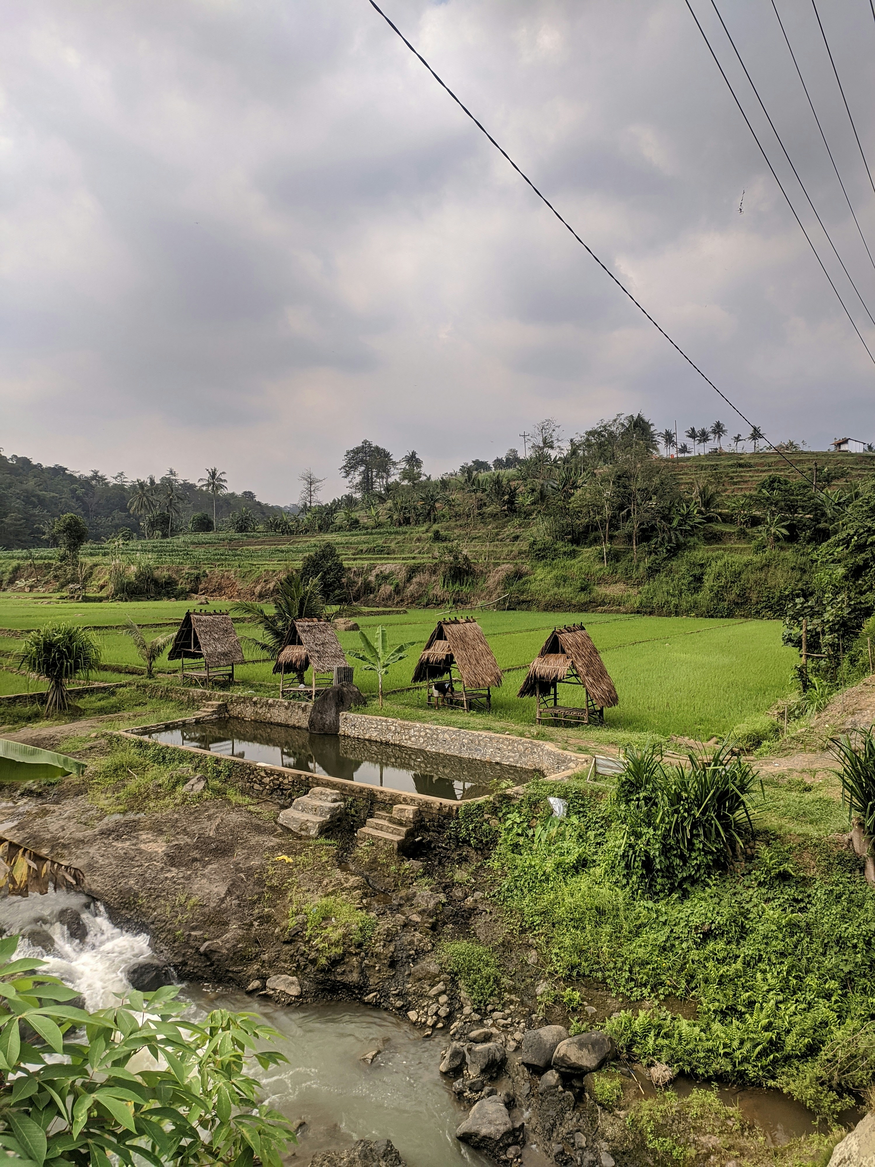 Lapangan rumput hijau dekat sungai di bawah langit mendung pada siang hari
