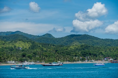 white boat on sea near green mountain under white clouds and blue sky during daytime