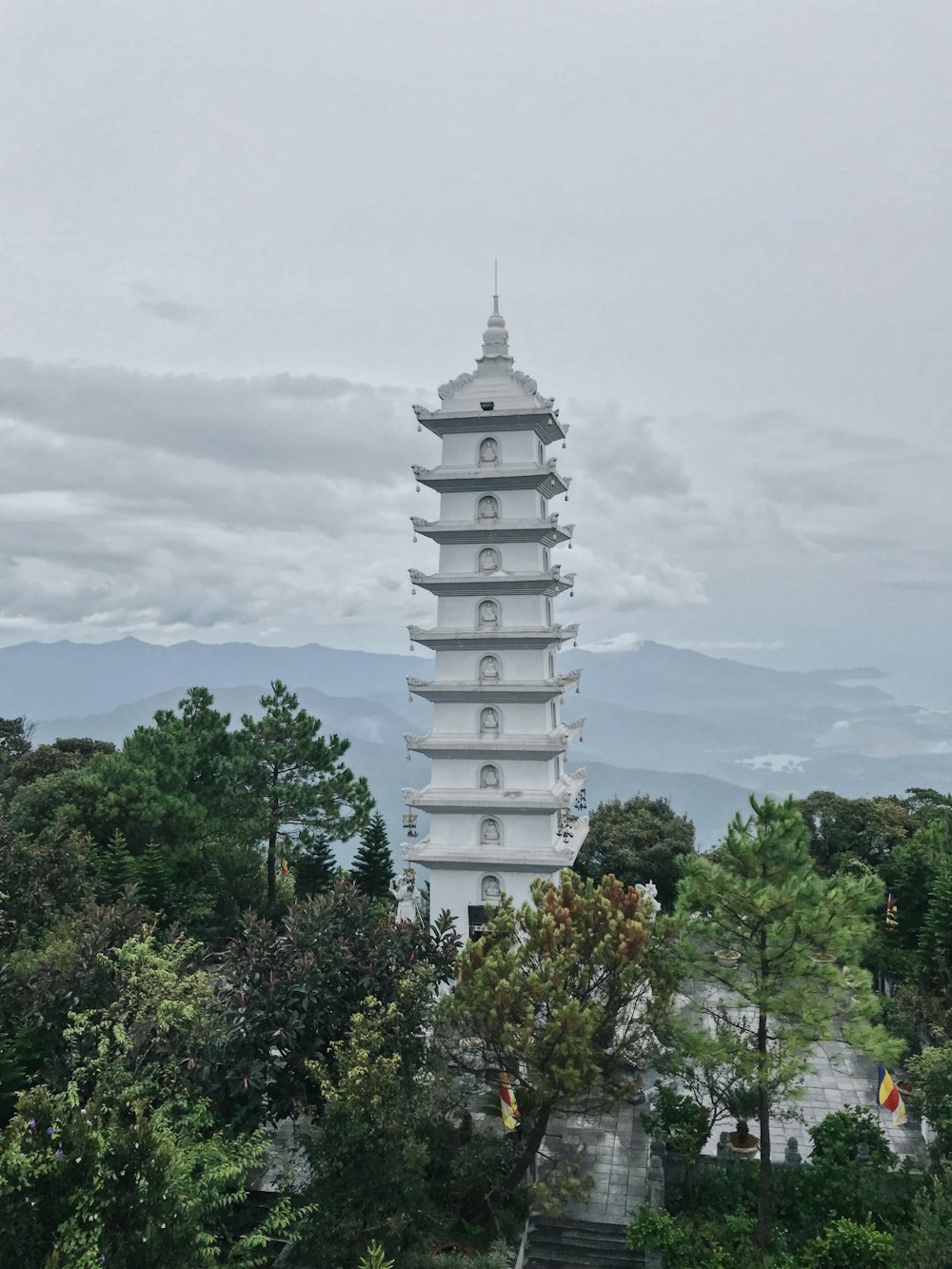 white concrete tower surrounded by green trees under white clouds during daytime