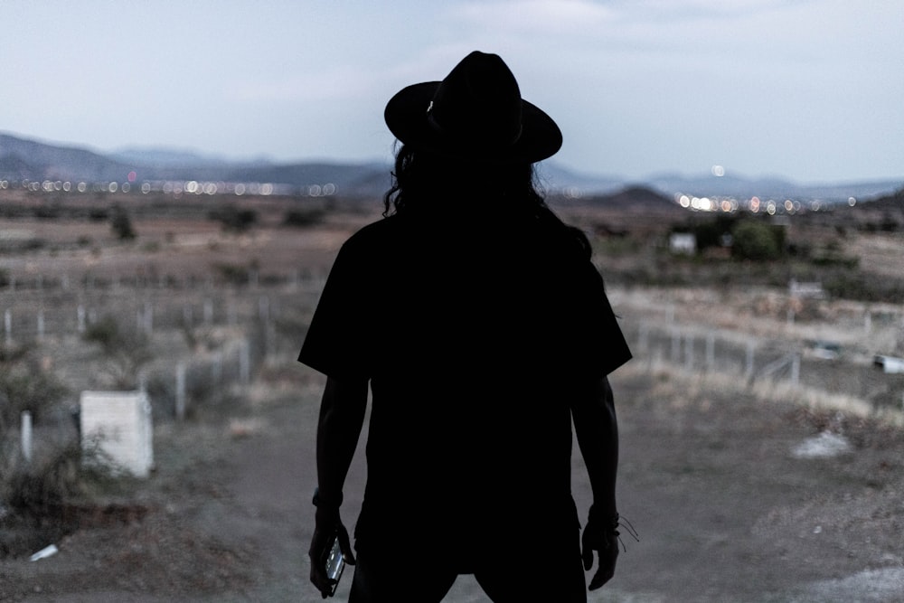 person in black hat standing on brown field during daytime