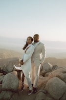 man in white suit standing beside woman in white dress on rock during daytime