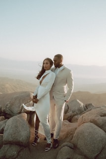 man in white suit standing beside woman in white dress on rock during daytime