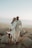 man in white suit standing beside woman in white dress on rock during daytime