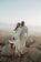 man in white suit standing beside woman in white dress on rock during daytime