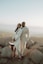 man in white suit standing beside woman in white dress on rock during daytime