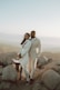 man in white suit standing beside woman in white dress on rock during daytime
