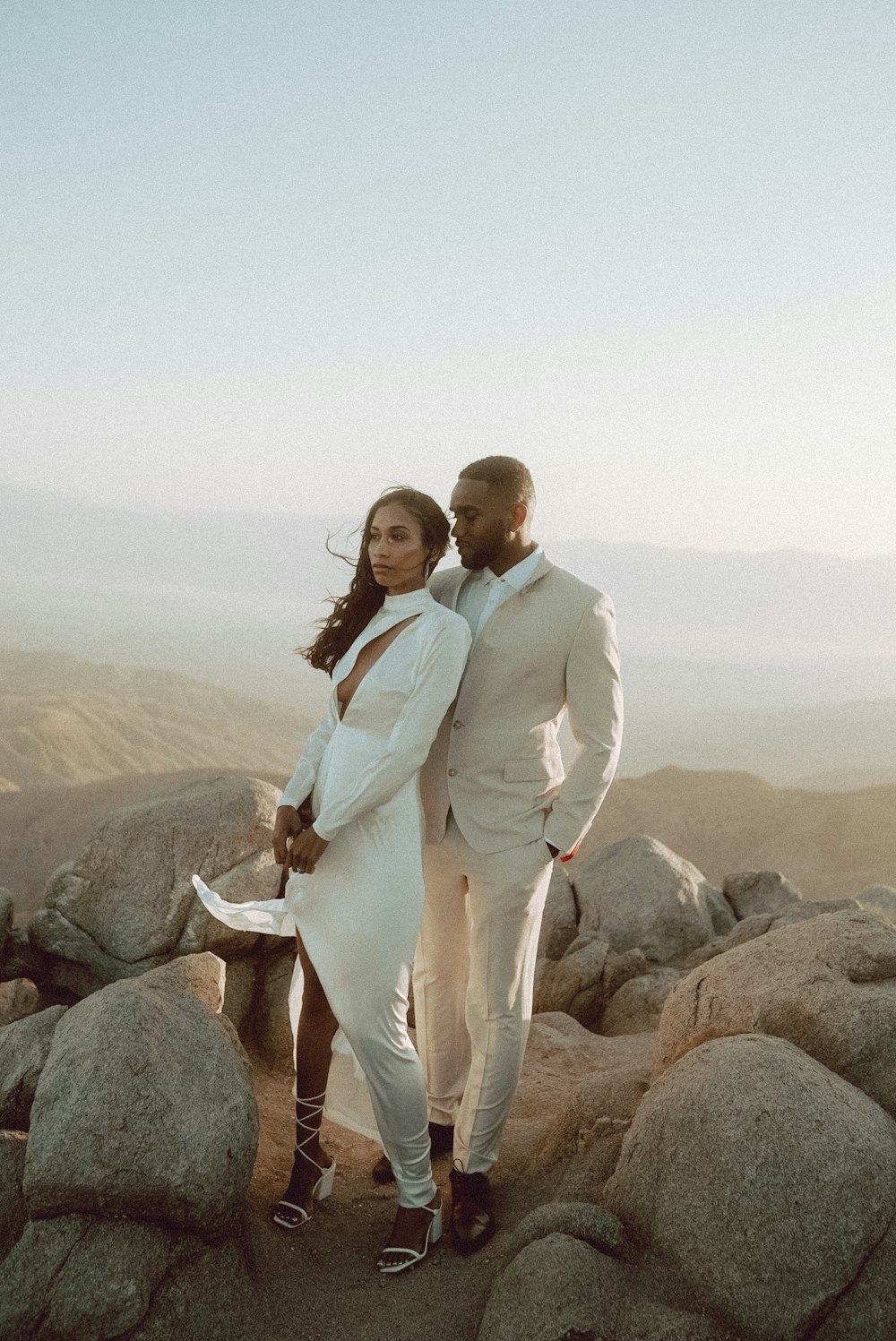man in white suit standing beside woman in white dress on rock during daytime
