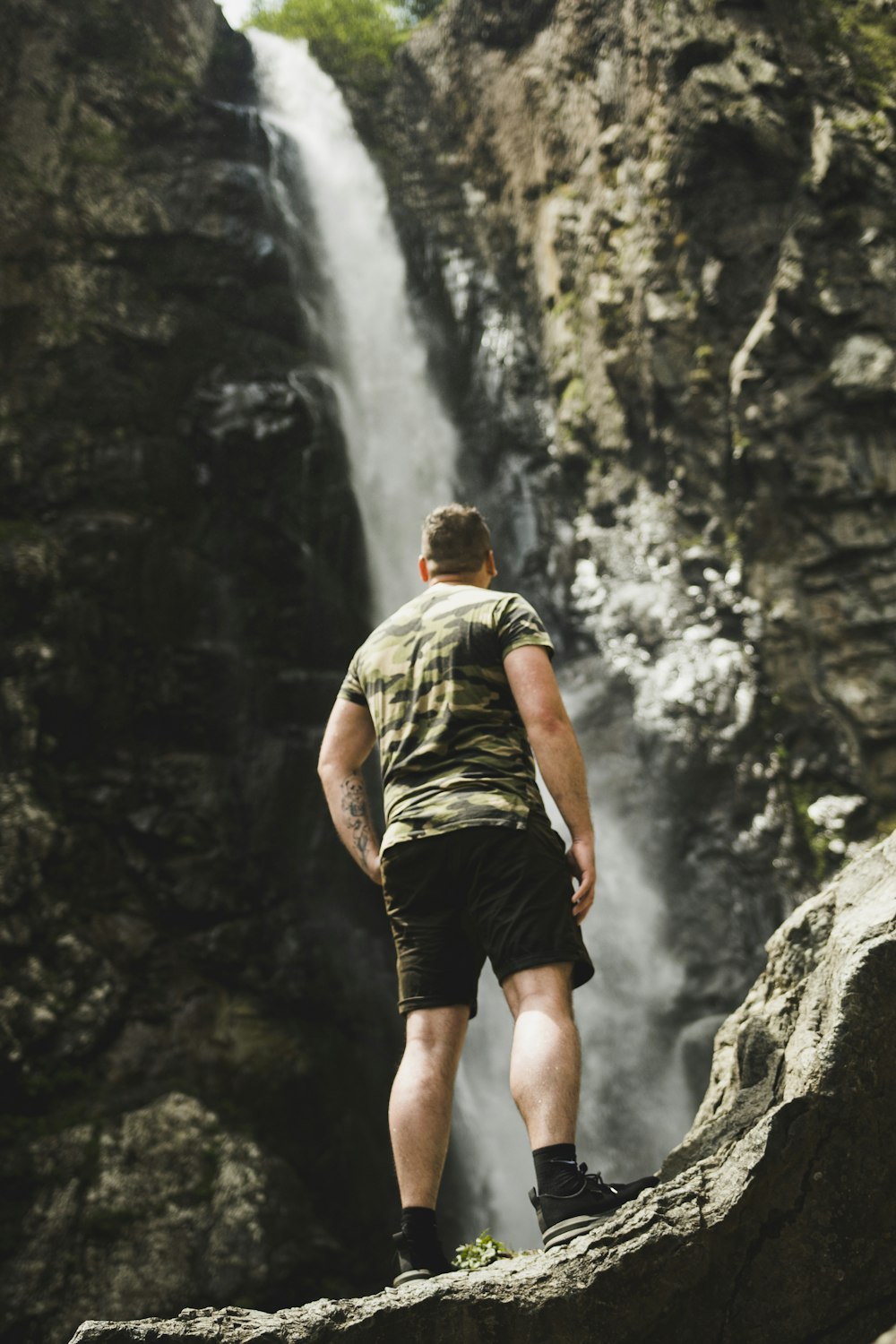 man in green t-shirt and black shorts standing on rocky mountain during daytime