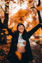 A joyful woman in her 50s laughing outdoors surrounded by colorful autumn leaves.