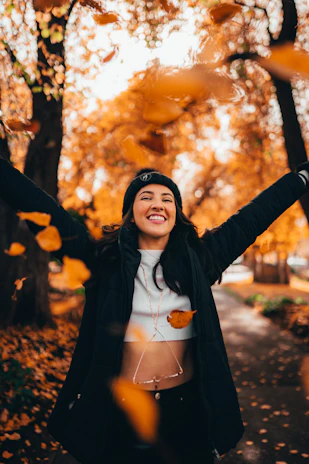 A joyful woman in her 50s laughing outdoors surrounded by colorful autumn leaves.