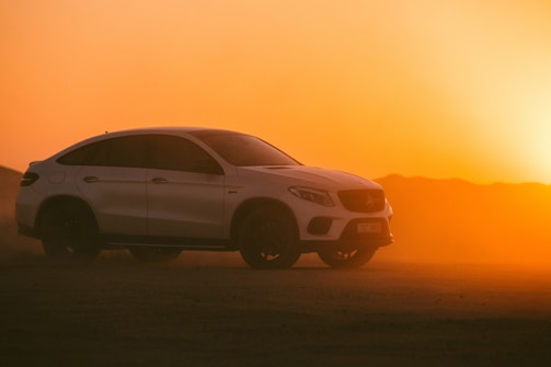 A sleek white rental car parked by a scenic desert road at sunset