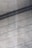 A textured concrete surface with fine grooves and scattered small holes. Diagonal shadows cast across the surface add depth and a sense of dimension.